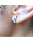Gold baguette emerald and diamond stud earring on an ear.