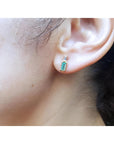 Minimalist 14K gold stud earring with baguette emerald and tapered diamond accents on an ear.