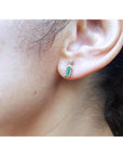 Minimalist 14K gold stud earring with baguette emerald and tapered diamond accents on an ear.