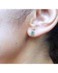 Minimalist 14K gold stud earring with baguette emerald and tapered diamond accents on an ear.