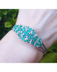 Bangle with emerald and diamonds on a wrist against a natural background.