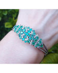 14k white gold bangle bracelet with prong-set round Colombian emeralds and diamonds on a wrist.