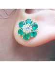 A 18k yellow gold diamond and emerald cluster earring on an ear.