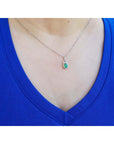 Pear-shaped Colombian emerald and diamond halo pendant on a delicate 14K white gold chain, worn on a blue shirt.