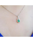 White gol necklace with a teardrop emerald pendant on a person wearing a blue top.