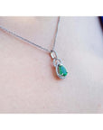 Pear-shaped Colombian emerald and diamond halo pendant in 14K white gold on a delicate chain.