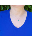 Pear-shaped Colombian emerald and diamond halo pendant on a 14K white gold chain, worn on a woman's neck.