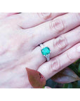 A cushion cut emerald ring on a hand with a natural background.