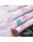 18K white gold ring with cushion cut emerald and trapezoid side diamonds on a hand.