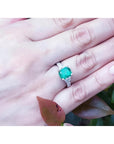 18K white gold ring with cushion cut emerald and trapezoid side diamonds on a hand.