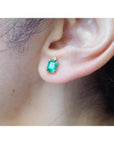 Rectangular Colombian emerald and diamond stud earring in 14K yellow gold on an ear.