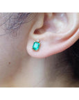 Rectangular Colombian emerald and diamond stud earring in 14K yellow gold on an ear.