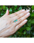 14K yellow gold stud earrings with rectangular Colombian emeralds and accent diamonds, worn on a hand.