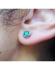 An ear wearing an emerald and diamond tulip stud earring in white gold.