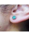 An ear wearing an emerald and diamond tulip stud earring in white gold.