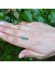 Emerald and diamond tulip stud earrings in 14K white gold, shown on a hand against green foliage.