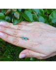 Emerald and diamond tulip stud earrings in 14K white gold, shown on a hand against green foliage.