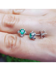Emerald and diamond tulip stud earrings in 14K white gold, featuring deep bluish-green emeralds and accent diamonds.