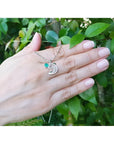 14K white gold dolphin pendant necklace with a brilliant round Colombian emerald on a hand.