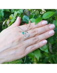 14K white gold dolphin pendant necklace with a brilliant round Colombian emerald on a hand.