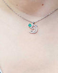 A round cut emerald dolphin pendant on a person's neck.