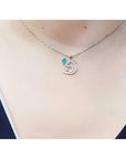 14K white gold dolphin pendant necklace with a deep green emerald and brilliant accents on a woman's neck.