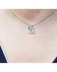 14K white gold dolphin pendant necklace with a deep green emerald and brilliant accents on a woman's neck.
