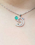 Necklace with a dolphin pendant with emerald and diamonds on a person's neck.
