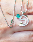A natural round cut emerald dolphin pendant with diamonds in white gold on a person's fingers.