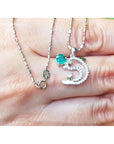 A natural round cut emerald dolphin pendant with diamonds in white gold on a person's fingers.