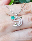 A 14K Solid white gold emerald dolphin pendant on a hand.