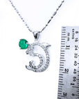 A Colombian emerald dolphin pendant next to a ruler on a white background