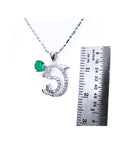 A Colombian emerald dolphin pendant next to a ruler on a white background