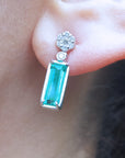 Close-up of a diamond and emerald earring on an ear with a blurred background