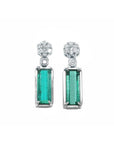 14K white gold dangling earrings with rectangular emeralds and diamond clusters.