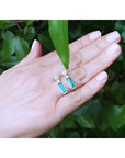 Emerald dangling earrings with diamond clusters in 14K white gold, displayed on a hand.