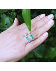 Emerald dangling earrings with diamond clusters in 14K white gold, displayed on a hand.