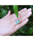 Emerald dangling earrings with diamond clusters in 14K white gold, displayed on a hand.