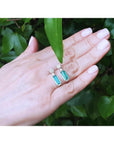 Emerald dangling earrings with diamond clusters in 14K white gold, displayed on a hand.