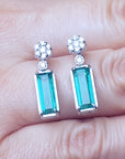 Pair of emerald-cut natural emerald earrings on a hand, full top view