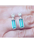 14K white gold dangling earrings with rectangular emeralds and diamond clusters.