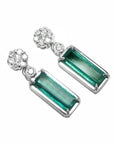 Pair of earrings with rectangular emeralds suspended fron a cluster diamonds accents on a white background