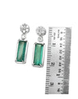 14K white gold dangling earrings with rectangular emeralds and diamond clusters, shown with a ruler.