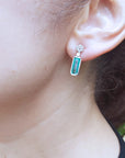 Close-up of a woman's face wearing a natural emerald earring with a blurred background