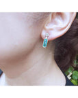 14K white gold dangling earrings with rectangular emeralds and diamond clusters on an ear.