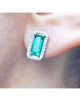 An emerald earring with halo diamond in 18k white gold on a earlobe