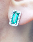 close up of an emerald earring with halo diamond in white gold on a earlobe