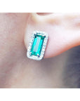 close up of an emerald earring with halo diamond in white gold on a earlobe