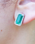 Natural emerald and diamond stud earrings on a person's ear