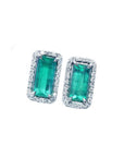 Emerald-cut Colombian emerald stud earrings with diamond halo in 18K gold.